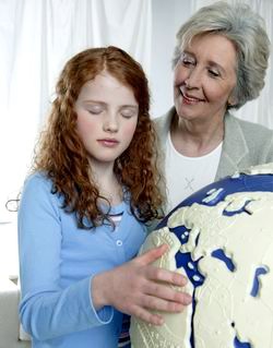 Una niña con los ojos cerrados toca un globo terráqueo en relieve para reconocer e identificar los continentes y sus formas.